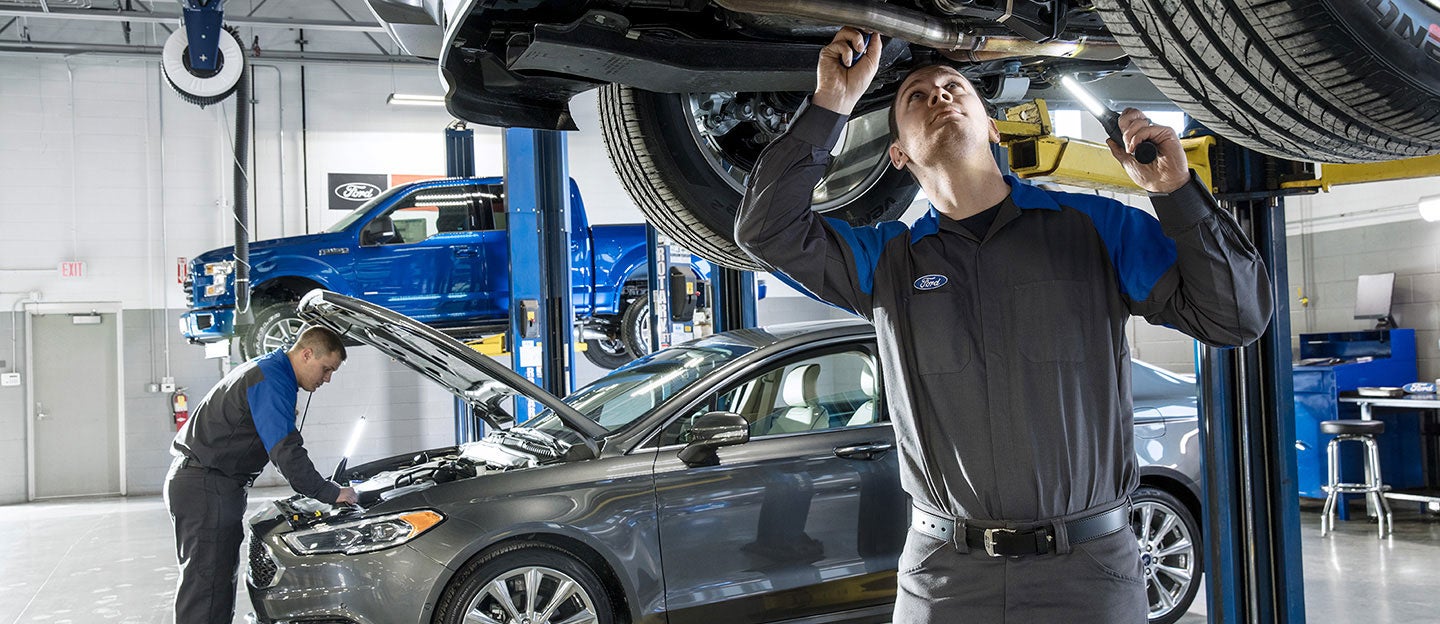 Two Ford service technicians beside vehicles in a service workshop