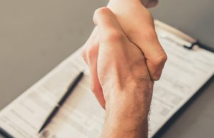 Two hands shaking over a clipboard with Ford Warranty paperwork